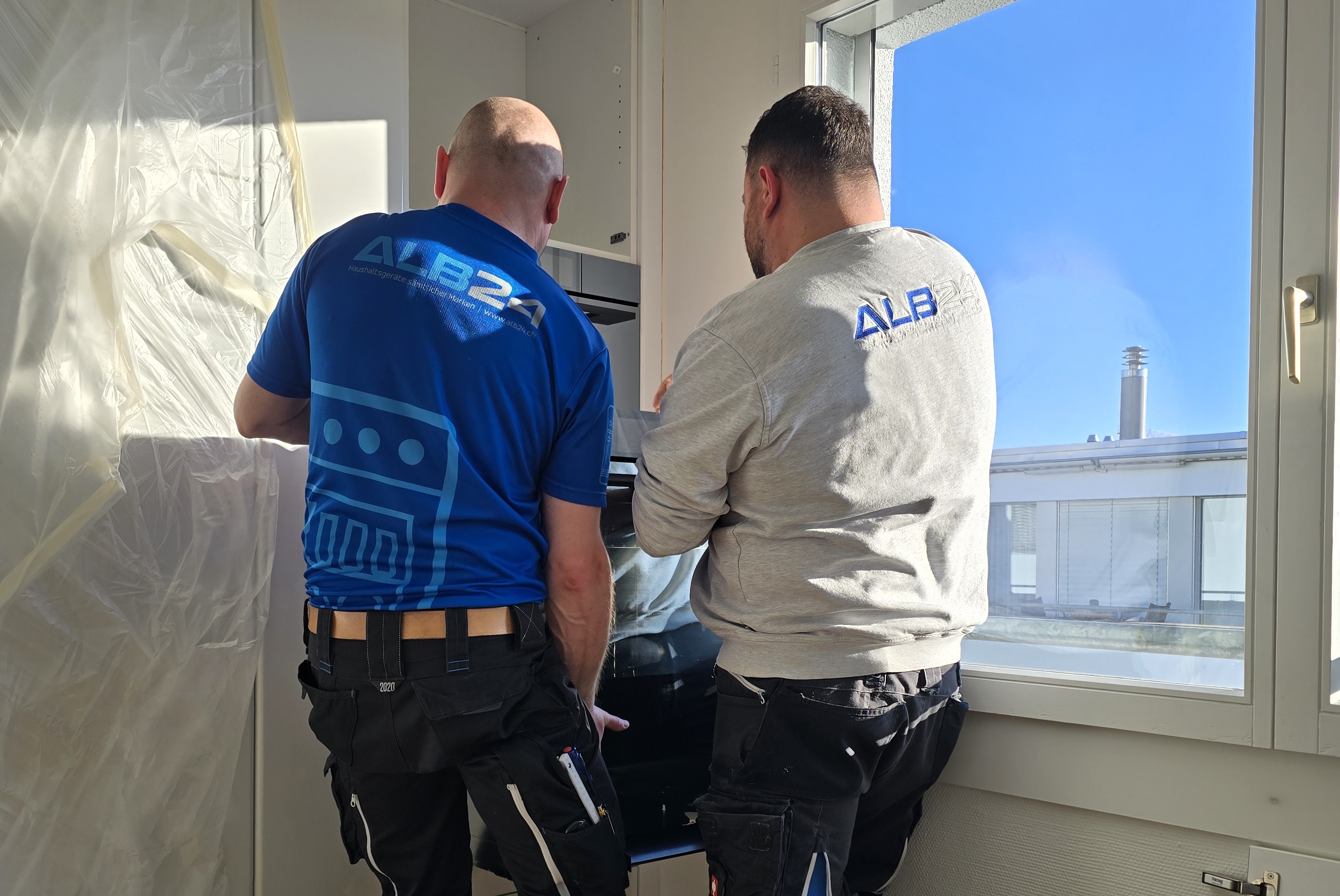 Zwei Monteure der ALB24 GmbH montieren ein Einbaugerät in einer Küche und instruieren die Kundschaft