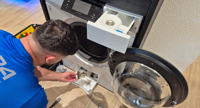 Techniker der ALB24 GmbH reinigt das Flusensieb einer Waschmaschine beim Kundenbesuch