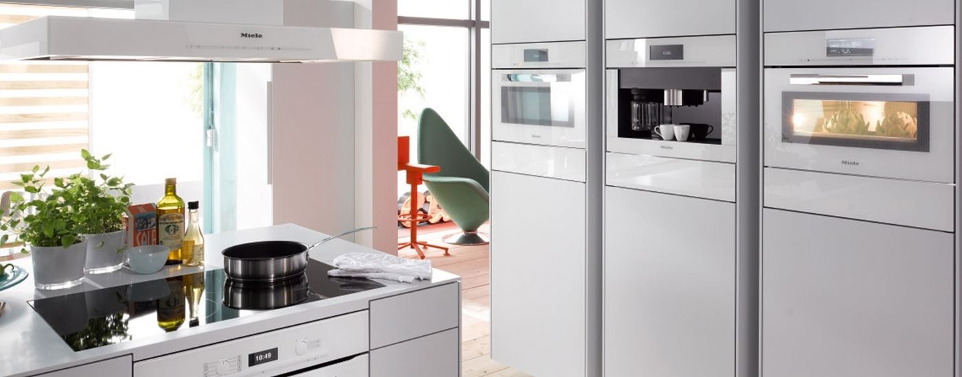 Helle moderne Küche mit weissen Einbaugeräten: Backofen, Dampfgarer und Kaffeecenter im Hochschrank sowie Induktionskochfeld mit Dunstabzug in der Kochinsel