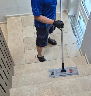 ALB24 Mitarbeiter im blauen Arbeitsshirt reinigt mit einem Flachmopp die Treppenstufen in einem Mehrfamilienhaus