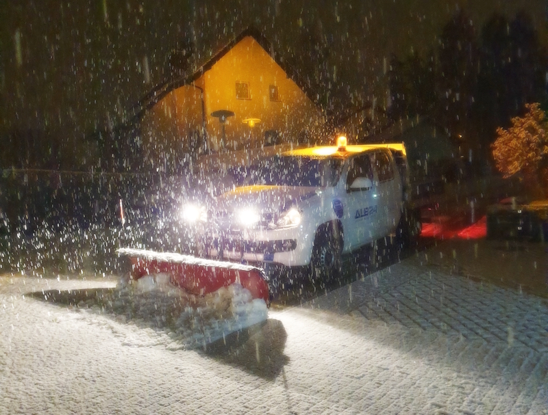 Fahrzeug der ALB24 GmbH mit Schneepflug räumt nachts bei dichtem Schneefall